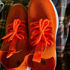 Orange sneakers med vit sula - Snygga och färgglada orange sneakers med vit sula och matchande snörning. Perfekta för en sportig look eller en promenad i stan. Storlek 40.