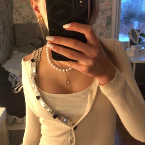 Beige kofta med paljettdetaljer - Snygg beige kofta med paljettdetaljer längs knäppningen. Perfekt för att lägga till lite glitter i vardagen. Koftan har en normal passform och långa ärmar. Tappat en knapp o några sitter lite löst, men går att fixa!