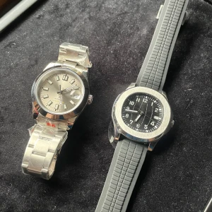 2 st Automatiska klockor - Säljer två stiliga herrklockor i en deal. Den ena har en silverfärgad urtavla med metallarmband och den andra en svart urtavla med gummiarmband. Båda har tydliga markeringar och en klassisk design. Perfekta för den som vill ha en tidlös look. Klockorna drivs av ett automatiskt urverk igen seiko och har Safirglas runtom. 