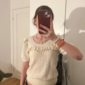 Beige stickad topp från & Other Stories - Säljer en söt beige stickad topp från & Other Stories. Toppen har korta ärmar och volangdetaljer vid halsringningen. Perfekt för en stilren look med en touch av romantik. 💫