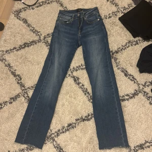 Blå jeans från Vero Moda - Snygga blå jeans från Vero Moda med klassisk femficksdesign och knappgylf. Perfekta för en avslappnad stil med en rak passform som ger en tidlös look. Har klippt benen!! Jag är 153 och de går hela vägen ner till golvet.