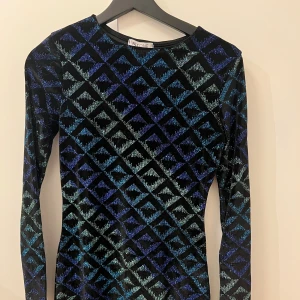 Mönstrad klänning från NELLY - Snygg klänning i sammet från NELLY med  mönster i glitter . Klänningen är kort och har en tight passform och långa ärmar, perfekt för en kväll ute. Endast använd 1 gång