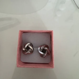 Snygga silverfärgade örhängen i knutdesign - Säljer ett par stilrena silverfärgade örhängen med en unik knutdesign. Perfekta för att ge en elegant touch till din outfit. De är lätta att bära och passar till många olika stilar. Obs! Jag rengjorde örhängena efter att andra bilden var tagen! Säljer eftersom att jag är en guldtjej. Nypris: 250kr