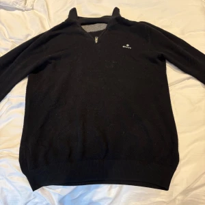 Svart tröja med dragkedja från Gant - Säljer en stilren svart halv zip tröja från Gant. Tröjan har en diskret logga på bröstet och är perfekt för kyligare dagar. Den är tillverkad i ett mjukt material och har långa ärmar.