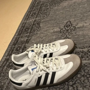 Adidas Samba sneakers - Snygga Adidas Samba sneakers i vitt och svart med klassiska ränder. Skorna har snörning och en stilren design med mockadetaljer på tån. Perfekta för en sportig look. Tyvärr för små för mig använda några enstaka gånger.