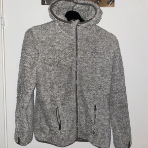 Grå fleecejacka - Mysig grå fleecejacka från On The Peak med huva och dragkedja framtill. Jackan har långa ärmar och två praktiska fickor med dragkedja. Perfekt för kyliga dagar.