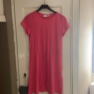 Rosa klänning från Vila - Säljer en söt rosa klänning från Vila i storlek S. Klänningen har korta ärmar och en enkel design med en knytning i midjan för en smickrande passform. Perfekt för en avslappnad och stilren look. Har bara använt den en gång så klänningen är i mycket bra skick💝