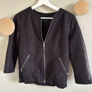 Svart jacka från rut & circle  - Snygg svart jacka med dragkedja framtill och två fickor med dragkedjor. Jackan har en stilren design med långa ärmar och ribbad nederkant. Perfekt för en cool och avslappnad look.