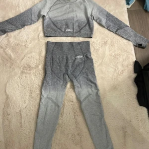 Grå ombre träningsset från ECHT - Säljer ett snyggt grått ombre träningsset från ECHT. Setet består av en croppad långärmad topp och matchande tights. Perfekt för gymmet eller yoga! Materialet är mjukt och stretchigt för bästa komfort. Topp har storlek L och tights M