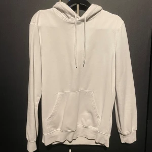 Vit hoodie från H&M - Säljer en stilren vit hoodie från H&M i relaxed fit. Den har en klassisk design med huva och dragsko samt en praktisk magficka. Perfekt för en avslappnad look.