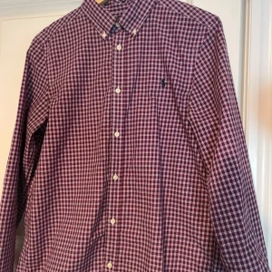Rutig skjorta från Ralph Lauren - Snygg rutig skjorta från Ralph Lauren i rött, blått och vitt. Skjortan har långa ärmar och knappar framtill. Den är broderad med den klassiska logotypen på bröstet. Perfekt för en stilren look!