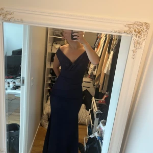 Mörkblå långklänning balklänning  - Elegant mörkblå långklänning med omlott-design och offshoulder-stil. Perfekt för formella tillfällen med sin smickrande passform och stilrena look. Jätte fin till tex bal. Prislappen är kvar och helt ny och oanvänd. Från Bubbelroom. Priset går såklart att diskutera.
