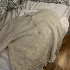 Beige kofta med knappar - Mysig beige kofta med knappar framtill. Perfekt för kyliga dagar med sin mjuka och bekväma passform. Ett stilrent plagg som passar till det mesta. Storleken är M men passar mig jätte fint som är en xxs/xs/S