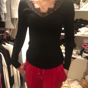 Svart långärmad topp med spetsdetaljer - Elegant svart långärmad topp med v-ringad spetsdetalj vid halsen. Perfekt för en stilren look. Aldrig använd.