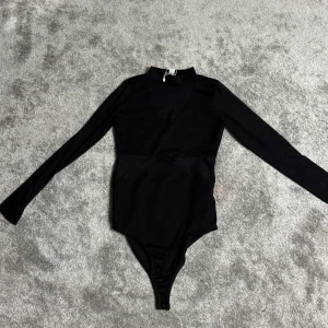 Svart långärmad bodysuit - Elegant svart långärmad bodysuit med hög krage. Perfekt för en stilren look, kan enkelt matchas med olika outfits. Materialet ser ut att vara mjukt och stretchigt för en bekväm passform.