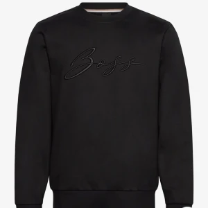 Svart sweatshirt från Boss - Helt oanvänd. Kommer i original förpackning. Ingen post bara mötes. Endast kontant. Snygg svart sweatshirt från Boss med broderad logga på bröstet. Tröjan har långa ärmar och en klassisk rund halsringning. Perfekt för en stilren look. NYPRIS: 2000kr