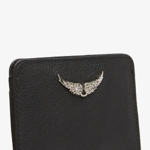 Svart plånbok  - Snygg och stilren svart plånbok i skinn med en elegant vingdetalj i silver på framsidan. Perfekt för att hålla dina kort organiserade med flera kortfack. En praktisk och trendig accessoar för alla tillfällen. Från Zadig o voltaire