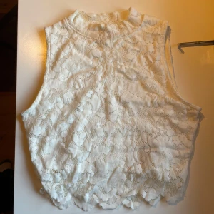 Vit spetslinne från FB Sister - Säljer ett vackert vitt spetslinne från FB Sister. Linnet är ärmlöst och har en elegant spetsdesign som ger en romantisk känsla. Perfekt för varma sommardagar eller som ett lager under en kavaj.