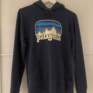 Mörkblå hoodie från Patagonia - Säljer en snygg mörkblå hoodie från Patagonia. Tröjan har en klassisk känguruficka och justerbar huva. Säljer då den är för liten för mig och inte kommer till användning längre🌄✨