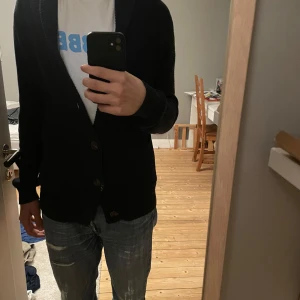 Mörkblå stickad kofta med knappar - Säljer en snygg mörkblå stickad kofta med knappar framtill. Perfekt för kyligare dagar och ger en stilren look. Koftan har långa ärmar och en bekväm passform.