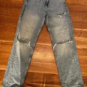 Blå jeans med slitningar från Gina tricot  - Säljer ett par coola blå jeans från Gina tricot  med slitningar på knäna och bakfickorna. De har en klassisk femficksdesign och knappgylf. Med medelhög midja storlek 36. Priset kan sänkas 