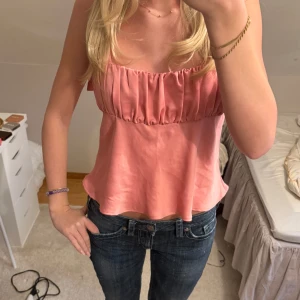 Rosa ärmlös topp - Säljer en söt rosa ärmlös topp med rynkad detalj vid bysten. Toppen har en luftig passform och tunna axelband, perfekt för varma dagar.