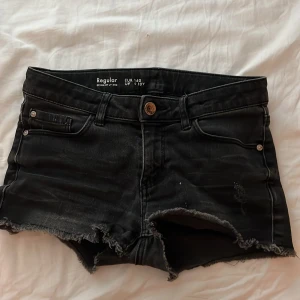 Svarta jeansshorts - Snygga svarta jeansshorts med slitna detaljer och fransig kant. Perfekta för en avslappnad stil. De har en knapp och dragkedja framtill samt klassiska fem fickor.