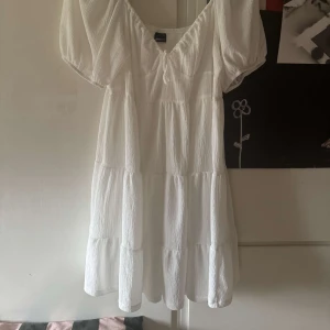 Vit klänning från Gina Tricot - Mycket bra skick använd 1 gång .Säljer en söt vit klänning från Gina Tricot med korta puffärmar och v-ringning. Klänningen har en luftig passform och är perfekt för varma dagar. Passar till studenten,midsommar eller skolavslutning. 