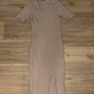 Beige ribbad klänning - Säljer en stilren beige ribbad klänning med korta ärmar. Klänningen har en enkel och elegant design som passar perfekt för olika tillfällen. Den är gjord i ett mjukt och bekvämt material.