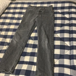 Grå jeansbyxor ifrån Levis  - Snygga grå jeansbyxor med klassisk femficksdesign. De har en rak passform och är perfekta för en avslappnad stil. Byxorna har en knapp och dragkedja framtill. Levis  501 