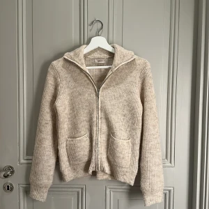 Beige stickad kofta från Only - Mysig beige stickad kofta från Only med dragkedja och huva. Perfekt för kyliga dagar. Koftan har långa ärmar och två praktiska fickor framtill. Aldrig använt! Köpte för 400kr