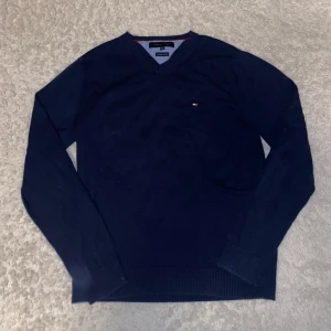 Tommy Hilfiger Tröja - Säljer en stilren mörkblå tröja från Tommy Hilfiger i premium bomull. Tröjan har en v-ringad design och långa ärmar, perfekt för en stilren look. Tröjan är i toppskick! Storlek M. Hör av er vid frågor👍👍