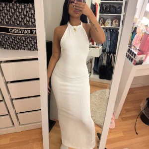 Vit långklänning med öppen rygg - Elegant vit långklänning med halterneck och öppen rygg. Klänningen har en tight passform och är perfekt för sommarens festligheter. Den är tillverkad i ett lätt och bekvämt material som ger en smickrande silhuett.