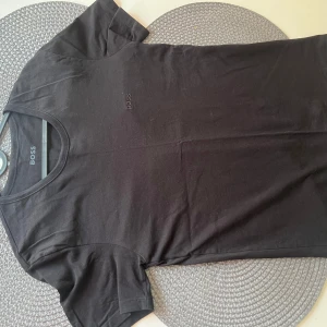 Svart t-shirt från Boss - Snygg oanvänd svart t-shirt från Boss med diskret logga på bröstet. Perfekt för en stilren look. Kortärmad och tillverkad i mjukt material. 