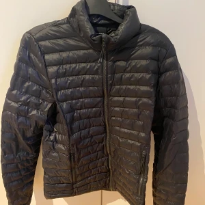Svart dunjacka från Everest - Säljer en svart dunjacka från Everest med dragkedja framtill. Jackan har en quiltad design och är perfekt till vår och höst. Den har långa ärmar och praktiska fickor med dragkedjor. En stilren och funktionell jacka för alla tillfällen.