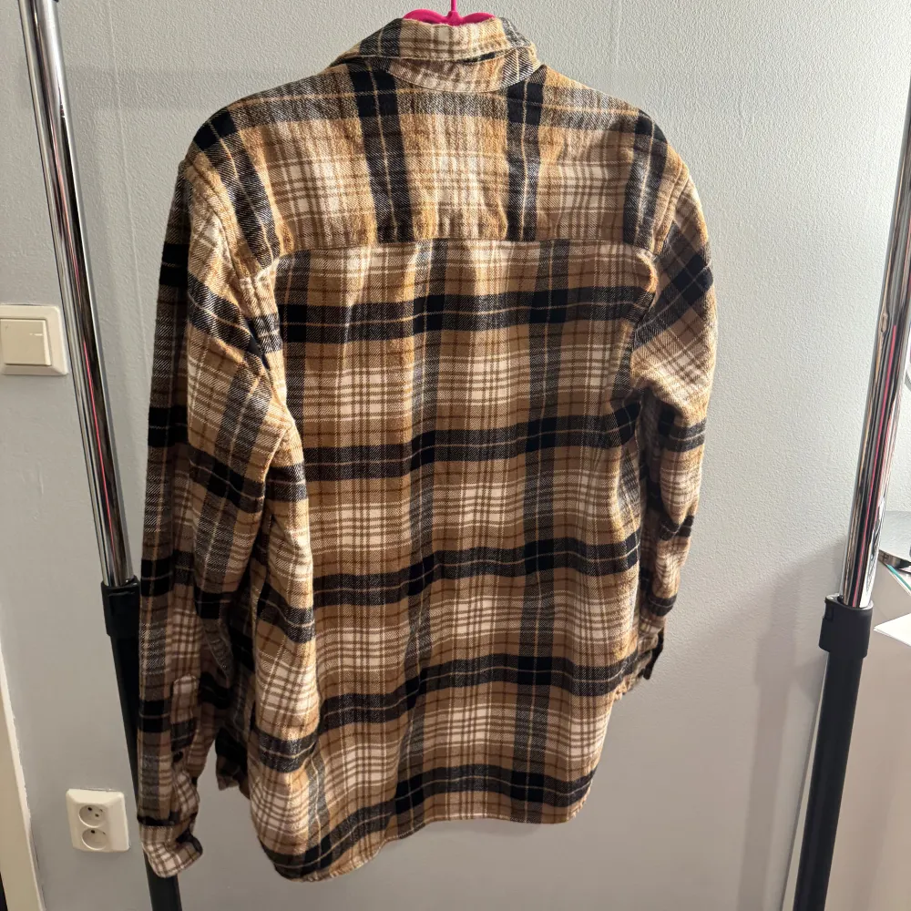 Säljer en snygg rutig skjorta från H&M i beige, svart och vit. Skjortan har långa ärmar och knappar framtill. Perfekt för lager-på-lager-stil och passar bra till både jeans och chinos.. Paidat.