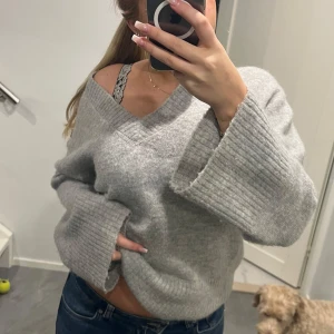 Grå stickad tröja från Gina Tricot - Mysig grå stickad tröja från Gina Tricot med v-ringning. Perfekt för kyligare dagar med sin mjuka och bekväma passform. Tröjan har långa ärmar och ribbade detaljer vid ärmslut och nederkant. Ett måste i garderoben för en stilren look.