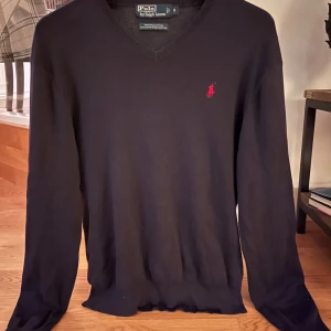 Svart tröja från Polo Ralph Lauren - Snygg mörkblå tröja från Polo Ralph Lauren i 100% pima bomull. Den har en v-ringad design med ett rött broderat märke på bröstet. Perfekt för en stilren look. Prutat och klart ✅ 