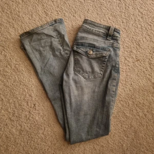 Blå lågmidjade bootcut jeans från Gina Tricot - Snygga blå lågmidjade bootcut jeans från Ginatricoti storlek 36. De har en femficksdesign med knappar på bakfickorna.