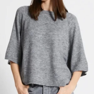 Grå stickad tröja - Säljer en mysig grå stickad tröja med trekvartsärm. Perfekt för kyligare dagar och enkel att matcha med olika outfits. Tröjan har en lös passform som ger en avslappnad look.