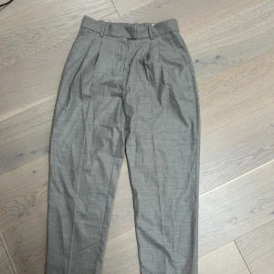 Grå kostymbyxor - Säljer ett par stiliga grå kostymbyxor i mycket bra skick. De har en klassisk design med veck framtill och en normal passform. 