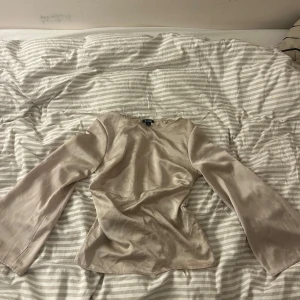 Beige satinblus från Boohoo - Säljer en elegant beige blus i satin från Boohoo. Blusen har långa ärmar och en mjuk, glansig yta som ger en lyxig känsla. Perfekt för både vardag och festliga tillfällen. Passar bra till både jeans och kjol!