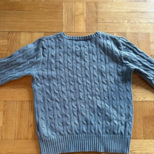 Grå stickad tröja från Polo Ralph Lauren - Säljer en snygg grå stickad tröja från Polo Ralph Lauren. Den har ett klassiskt flätmönster och är perfekt för både höst och vinter. Tröjan är långärmad med ribbade muddar vid ärmslut och nederkant. Supermysig och stilren!