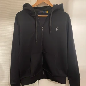 Ralph Lauren zip hoodie - Säljer en stilren svart hoodie från Polo Ralph Lauren i storlek Large. Perfekt för både vardag och chill. Den är i bra skick och redo för en ny ägare!
