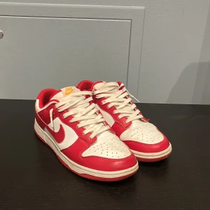 Nike Dunk i rött och vitt - Säljer ett par snygga Nike Dunk sneakers i rött och vitt. Skorna har en klassisk design med snörning och en bekväm passform. Skriv till mig angående eventuella frågor. Priset är inte hugget i sten!