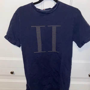 Mörkblå t-shirt från Les Deux - Snygg mörkblå t-shirt från Les Deux med ett stilrent tryck på framsidan. Perfekt för en avslappnad look. T-shirten har korta ärmar och en rund halsringning.