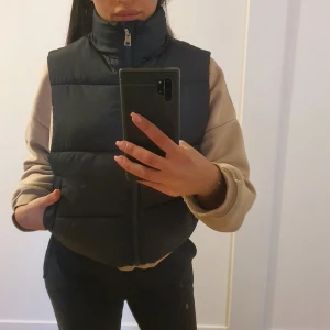 Svart dunväst - Säljer en svart dunväst i nytt skick. Västen har en dragkedja framtill och är perfekt för höst och vinter. Den är i storlek S och har en normal passform. Supermysig och varm för kyliga dagar!