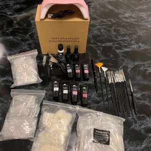 Nagelkit med LED-lampa och gellack - Komplett nagelkit med rosa LED-lampa för gelnaglar, flera färger av gelpolish från Nee Jolie, top coat och base coat. Inkluderar även nagelklippare och en uppsättning borstar för detaljerad applicering. Perfekt för hemmabruk eller salong! Oanvänt och i nyskick!
