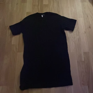 Lång Svart t-shirt från H&M Divided - Säljer en enkel och stilren svart t-shirt i längre modell från H&M Divided i storlek S. Perfekt basplagg för alla tillfällen. T-shirten är kortärmad och gjord i mjukt material för en bekväm passform. Passar både till vardags och fest!