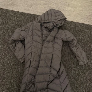 Svart dunjacka med huva - Snygg svart dunjacka från Tommy Hilfiger med huva. Jackan har ett quiltat mönster och långa ärmar. Perfekt för kyliga dagar.